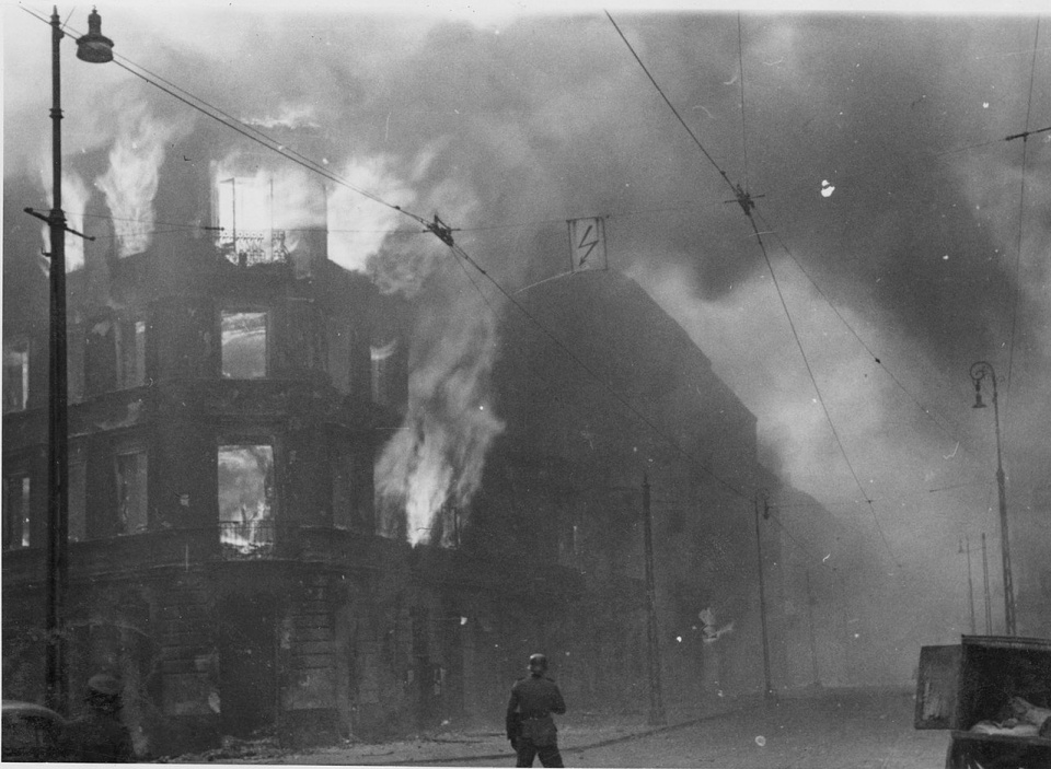 Fotografia z Raportu Stroopa. Płoną podpalone przez Niemców kamienice na skrzyżowaniu ulic Zamenhofa i Wołyńskiej [fot. wikipedia/domena publiczna]